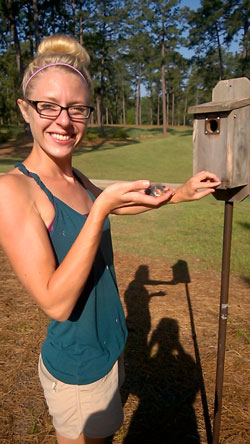Dr. Lauren Gillespie holding a bird next to a birdhouse
